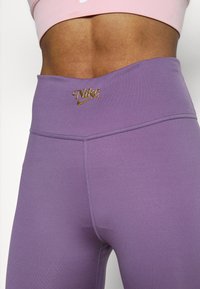 Violetit Nike-legginssit, joissa on korkeavyötäröinen vyötärö, kullanvärinen logo edessä sekä sileä, joustava kangas ja litteät saumat.