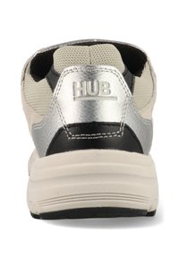 Sneaker met een zwarte en zilveren gestructureerde hak, lichtgrijze mesh bovenkant en een contrasterende zwarte tussenzool, met de merknaam "HUB" in reliëf.