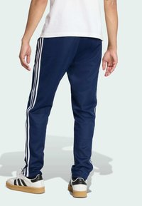 Ναυτικές φόρμες joggers με λευκές πλευρικές ρίγες. Φτιαγμένες από μαλακό ύφασμα, με στενή εφαρμογή και ελαστική μέση. Συνδυάζονται με μαύρα και λευκά αθλητικά παπούτσια.