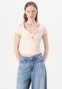 Top aderente di colore crema a maniche corte con dettaglio annodato sul davanti, abbinato a jeans azzurri a vita alta. Tessuto semplice e liscio.