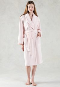Accappatoio rosa in peluche con colletto a scialle, cintura di legatura e due tasche frontali; presenta una texture morbida e una lunghezza midi.