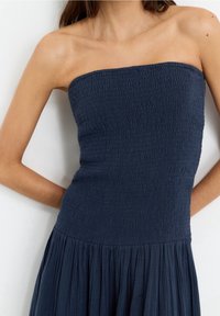 Robe bleu marine sans bretelles avec un corsage smocké et une jupe plissée. Texture douce avec un design fluide. Aucune décoration visible.