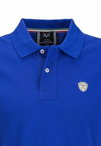 Koninklijkblauwe polo gemaakt van gestructureerde stof, met een kraag, twee witte knopen en een geborduurd schildlogo op de borst.