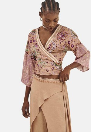 Blusa envolvente de mangas cortas en rosa con intrincados bordados florales y acentos de perlas, combinada con una falda beige de acabado texturizado.