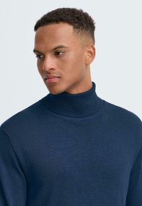 Jūras spēku turtlenecks džemperis, izgatavots no mīkstas auduma, ar augstu apkakli un gludu faktūru, pieguļošs dizains un minimāli savienojumi.
