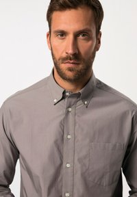 Chemise grise à col, dotée d'une poche poitrine et d'une texture subtile, fermée par des boutons de couleur claire.