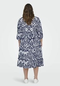 Mornarsko modra in bela obleka s potiskom, ki ima večstopenjski krilo, napihnjene rokave in mehak material, z zapletenimi geomatrskimi vzorci po celotni površini.