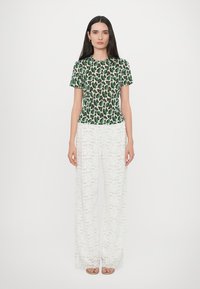 Top verde e bianco a manica corta con motivo, abbinato a pantaloni larghi bianchi in pizzo, caratterizzati da un tessuto testurizzato e un design floreale.