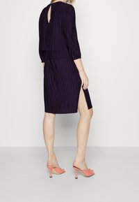 Lila plisserad klänning med trekvartslånga ärmar, en nyckelhålsrygg, sidofrid och matchad med persikofärgade öppna klackar. Slät tygyta.