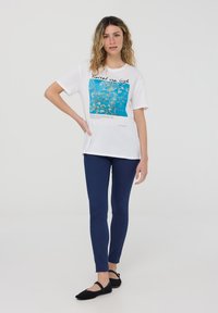 T-shirt bianca in cotone con stampa blu di Van Gogh, collo rotondo, maniche corte, abbinata a leggings blu navy e ballerine nere.