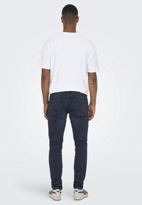 Camiseta de algodón blanca, vaqueros de denim azul y zapatos blancos. Los vaqueros presentan un corte slim y bolsillos traseros, con una textura sutil.