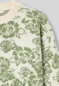 Pull en tricot avec un fond crème orné d'un motif floral vert texturé. Encolure côtelée et tissu doux. Coupe standard.
