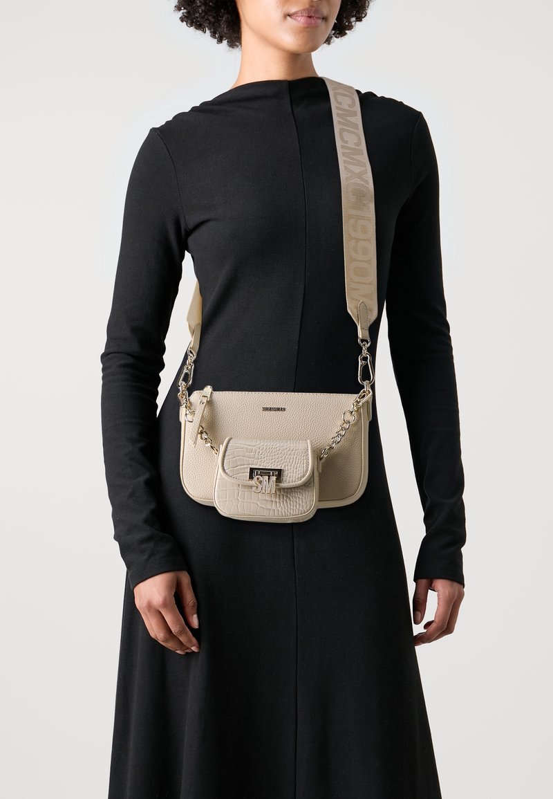 Beige crossbody bag made of textured leather, featuring a front pocket, silver hardware, and a strap with logo detail.