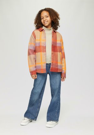 Veste à carreaux dans des teintes orange, rouge, beige et violette ; avec des boutons et un col. Associée à un jean bleu à jambe large et des baskets blanches.