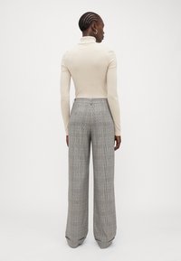 Maglione beige a collo alto con maniche lunghe abbinato a pantaloni grigi a gamba larga con motivo a quadri e vestibilità sartoriale.
