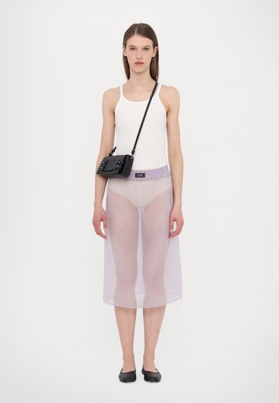 Top bianco senza maniche, gonna trasparente viola che arriva a metà polpaccio, borsa nera con tracolla regolabile, scarpe nere basse, stile minimalista.