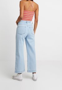 Jeans anchos de color azul claro con bolsillos traseros, combinados con una camiseta sin mangas de rayas rojas y blancas. Modelo llevando zapatillas altas blancas.