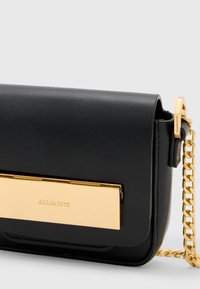 Borsa a tracolla in pelle nera con una chiusura rettangolare dorata, tracolla a catena e texture liscia. Presenta il nome del marchio impresso sulla chiusura.