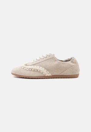 Baskets casual en daim beige avec semelle en caoutchouc, fermeture à lacets et bordure décorative tressée de couleur crème sur le côté.