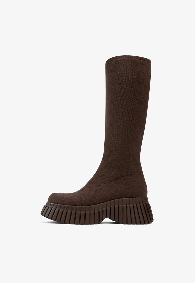 Botín de punto marrón oscuro y alto con suela de plataforma gruesa acanalada y punta redondeada, mostrado en perfil lateral sobre un fondo blanco.