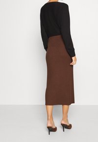 Femme portant une jupe midi côtelée marron, un haut à manches longues noir, et des mules à talons imprimé léopard, vue de dos.