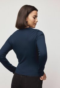 Navy long-sleeve shirt made from stretchy fabric, featuring a classic crew neckline and a fitted silhouette. Smooth texture enhances comfort.