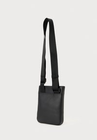 Black crossbody bag made of smooth synthetic material, featuring a rectangular shape, adjustable strap, and minimalist design.