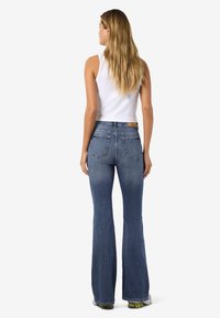 Traperice plavkaste boje s proširenim nogavicama i srednjim strukom, izrađene od trapera. Stražnji dio ima dva džepa i kožni umetak blizu struka.