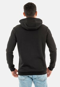 Hoodie noir avec une capuche à cordon, manches longues et poignets côtelés, associé à un jean en denim bleu clair. Texture lisse et coupe ajustée.