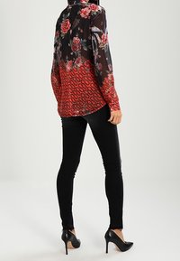 Blusa in chiffon floreale con un motivo rosso degradé nella parte inferiore, abbinata a jeans skinny neri e scarpe con tacco nere.