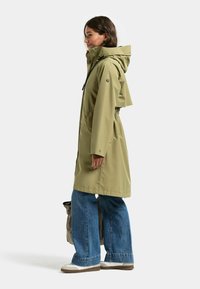 Wodoodporna kurtka w oliwkowej zieleni z kapturem, ściągaczem w pasie i zatrzaskami. Połączona z szerokimi niebieskimi jeansami i trampkami.