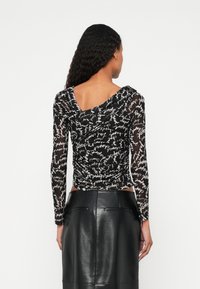 Must pikkade varrukatega pluus läbipaistva tekstuuriga, millel on paelutud disain ja valged käsitsi kirjutatud mustrid; kombineeritud kõrge vöökohtadega nahast seelikuga.