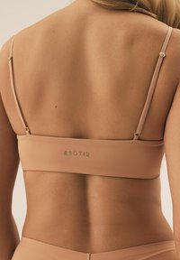 Beżowy, bezszwowy biustonosz braletka z cienkimi, regulowanymi ramiączkami, o gładkiej teksturze i złotym logo "ESOTIQ" na tylnej taśmie.
