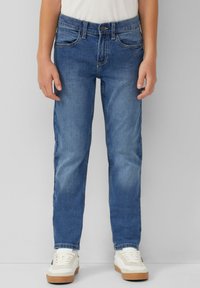 Modri denim kavbojki s ravnim krojem, svetlo pranje, pet žepov in kontrastnim šivanjem, v kombinaciji z belimi supergami in preprosto majico.