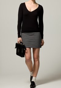 Top nero a maniche lunghe con scollatura a V, abbinato a una gonna a righe bianche e nere. Gli accessori includono una borsa nera e calze bianche.