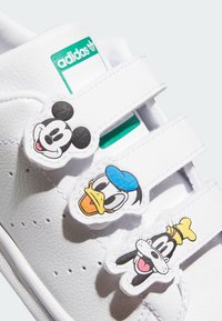 Sneakers bianchi con tre fasce in velcro, decorate con toppe di personaggi dei cartoni animati: Topolino, Paperino e Pippo. Materiale sintetico liscio.