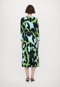 Šaty s výrazným abstraktním vzorem v zelených, modrých a černých odstínech. Dlouhé rukávy, definovaný pas a sukně do kolen. Hladká látka.