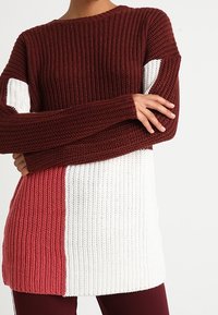 Pull en maille avec un design à blocs de couleurs en bordeaux, blanc et corail. Texture côtelée ; manches longues avec épaules tombantes.