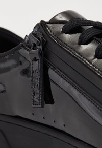 Μαύρο αθλητικό παπούτσι από πατεντ δέρμα με κλείσιμο με φερμουάρ και υφασμένες κορδόνες. Ξεχωριστή ετικέτα λογότυπου και λεία επιφάνεια με ελάχιστες λεπτομέρειες διάτρησης.