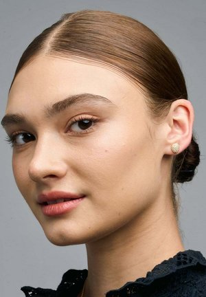Orecchini a bottone in oro con superficie texture, caratterizzati da una forma rotonda. I capelli del modello sono raccolti, mettendo in risalto gli orecchini.