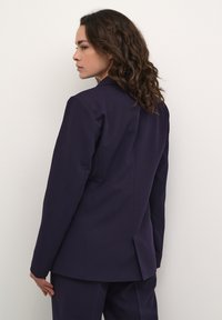 Námořnický blazer se strukturovaným designem, s jedním rozventem na zádech, střih na míru a hladkou tkaninou, doplněný o oblekové kalhoty ve stejném odstínu.
