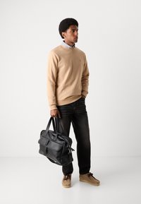 Sweatshirt beige, jeans en denim foncé et chaussures en suède marron. Sac en cuir noir avec poignées supérieures, comportant un rabat avant et une fermeture éclair.