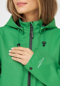 Chaqueta verde hecha de un tejido texturizado, con cierre frontal con cremallera, capucha ajustable y puños con botón con detalle de logo.