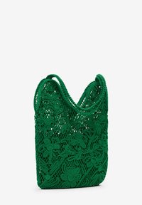 Grön virkad väska med intrikata blommönster, en mjuk textur och två runda handtag för enkel bärning.