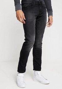 Pantalones vaqueros skinny negros de denim, con un lavado desgastado, cinco bolsillos y corte ajustado, combinados con zapatillas blancas.