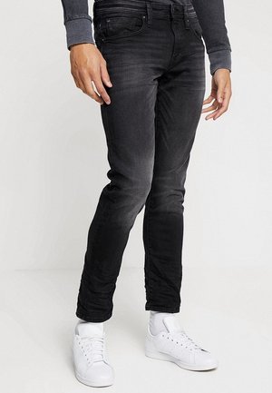 Pantalones vaqueros skinny negros de denim, con un lavado desgastado, cinco bolsillos y corte ajustado, combinados con zapatillas blancas.