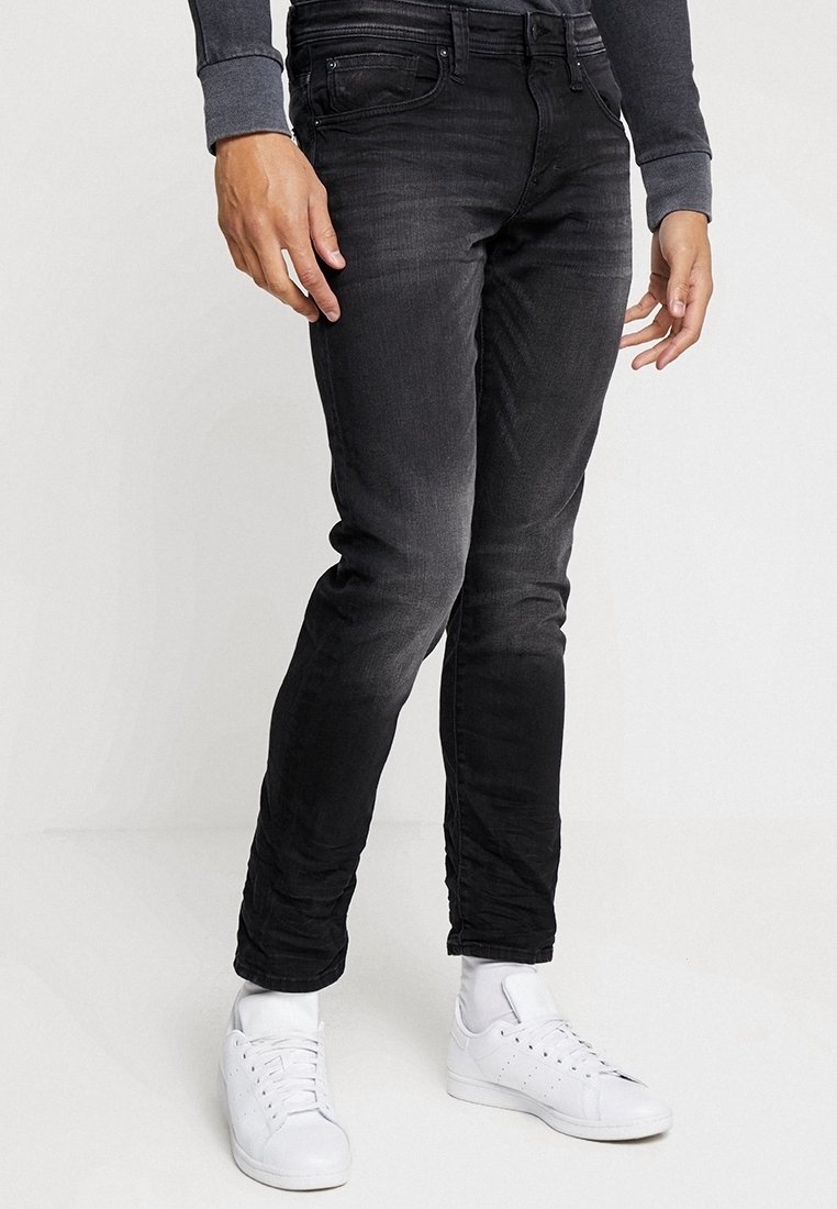 Pantalones vaqueros skinny negros de denim, con un lavado desgastado, cinco bolsillos y corte ajustado, combinados con zapatillas blancas.