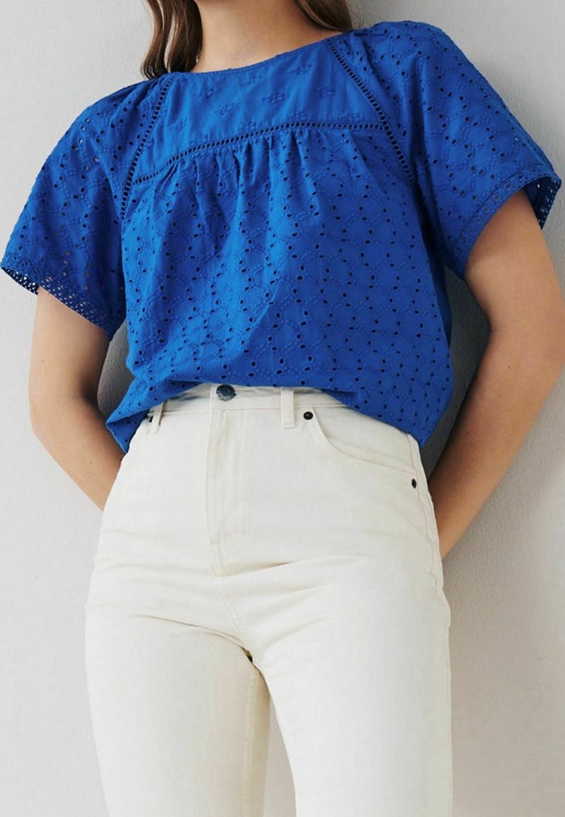 Top in cotone blu a maniche corte, con dettagli a occhiello e scollatura rotonda, abbinato a jeans bianchi a vita alta.