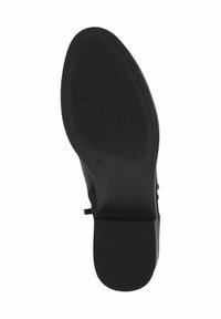 Suela de zapato negra con un patrón de agarre texturizado, forma ligeramente redondeada y tacón plano. Presenta un empeine suave y una trabilla en la parte trasera.