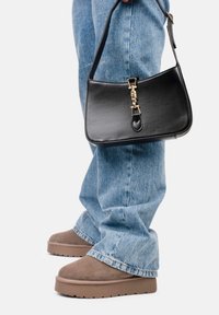 Bolso de piel negra con un diseño estructurado, herrajes dorados y un asa corta, combinado con unos vaqueros de denim azul claro y zapatos de plataforma marrones.